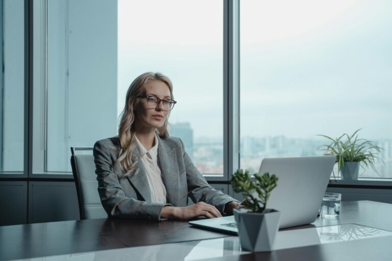 Confident businesswoman in grey suit working on laptop in modern office