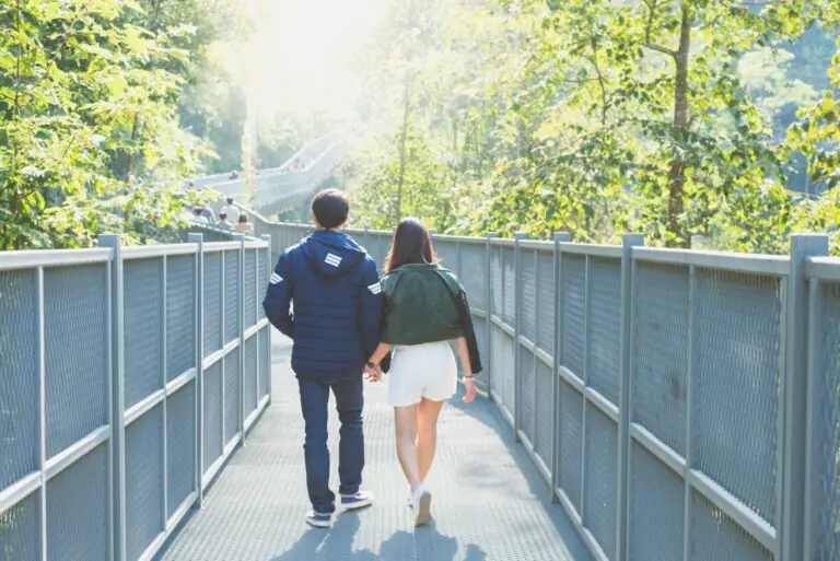 Couple walking together through lush forest on sunlit nature pathway.
