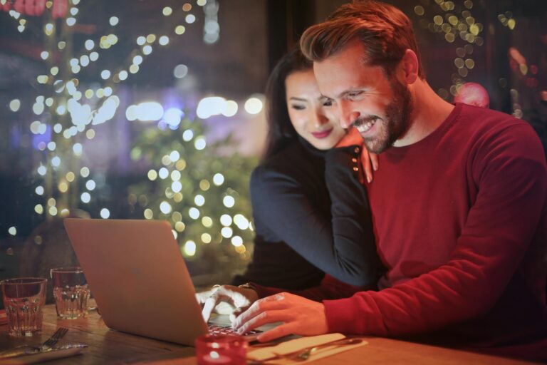 Couple using laptop at cozy restaurant with festive bokeh lights shopping online