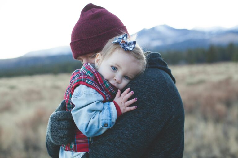 Father and child embrace outdoors with winter mountain backdrop.