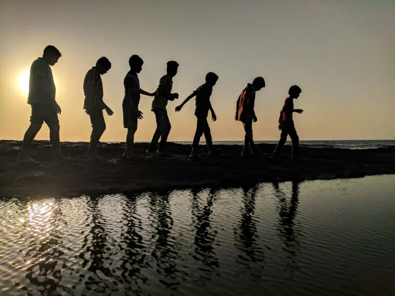 Group of children walking along shoreline silhouetted against sunset reflection