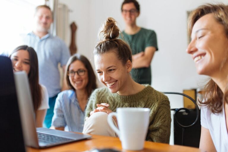 Group of friends smiling indoors watching video together on laptop.