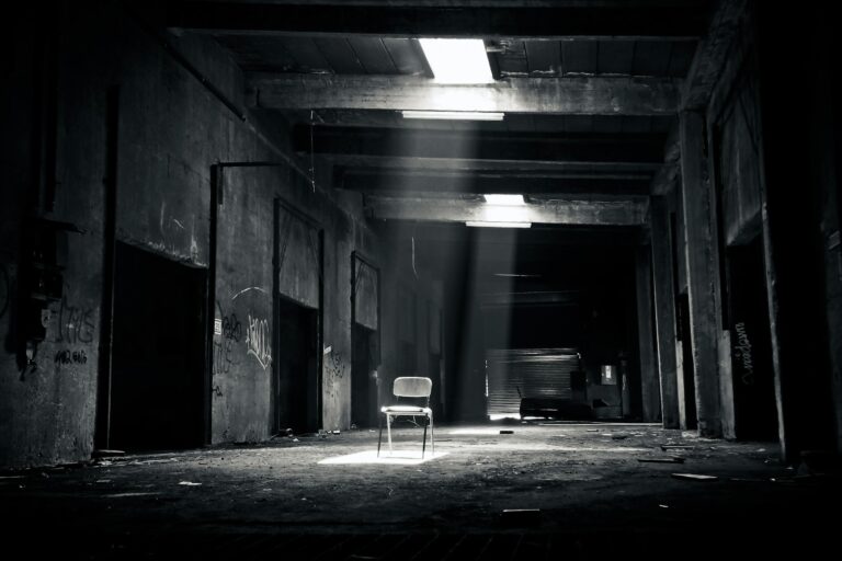 Black and white abandoned warehouse with solitary chair lit by sunlight.