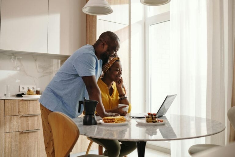 Happy couple sharing breakfast and working on laptop in cozy kitchen