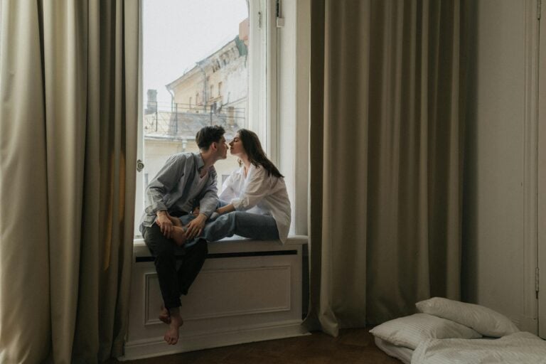 Loving couple sharing tender kiss on cozy indoor windowsill.