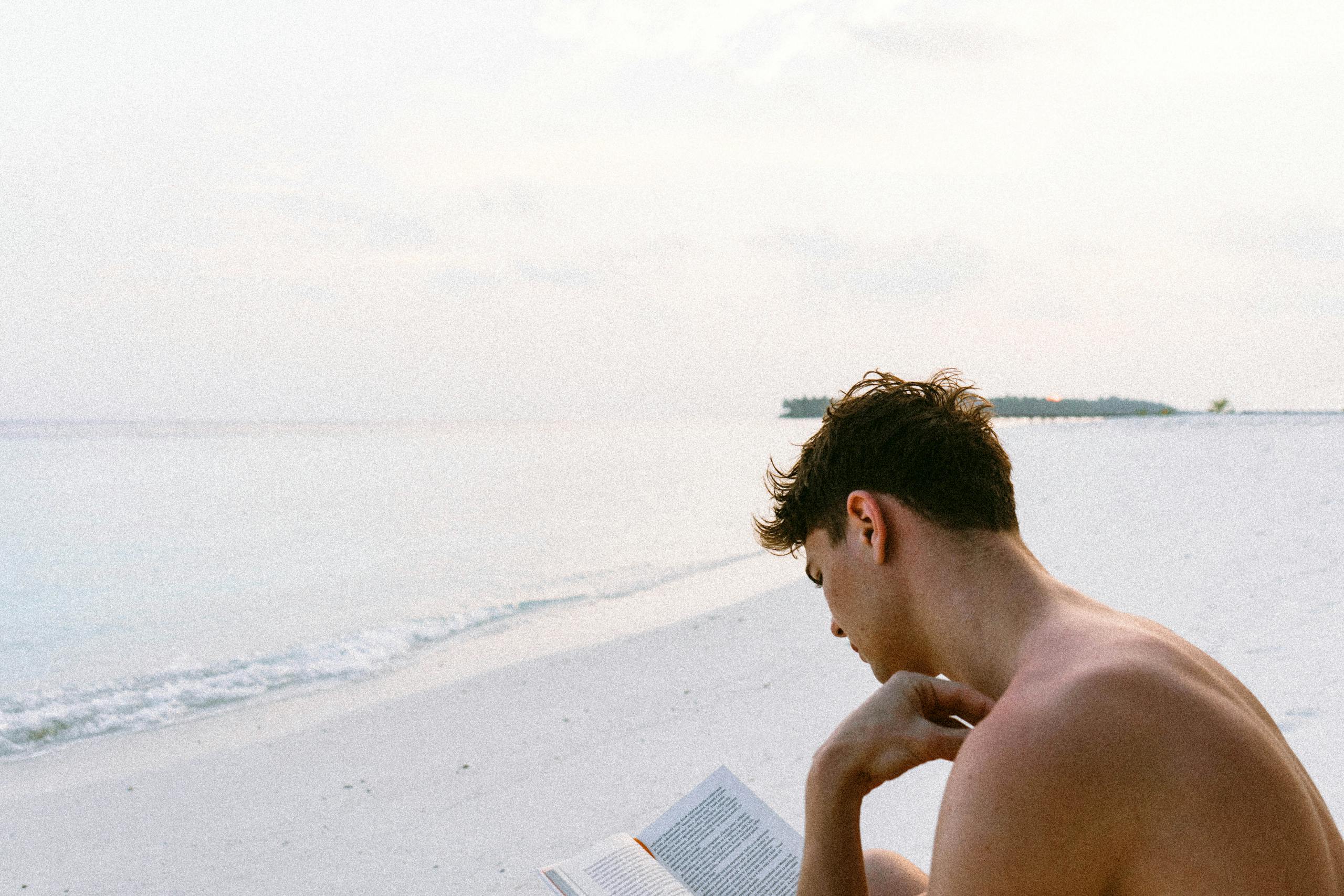 Man contentedly reading book on serene beach in Maldives capturing relaxation essence