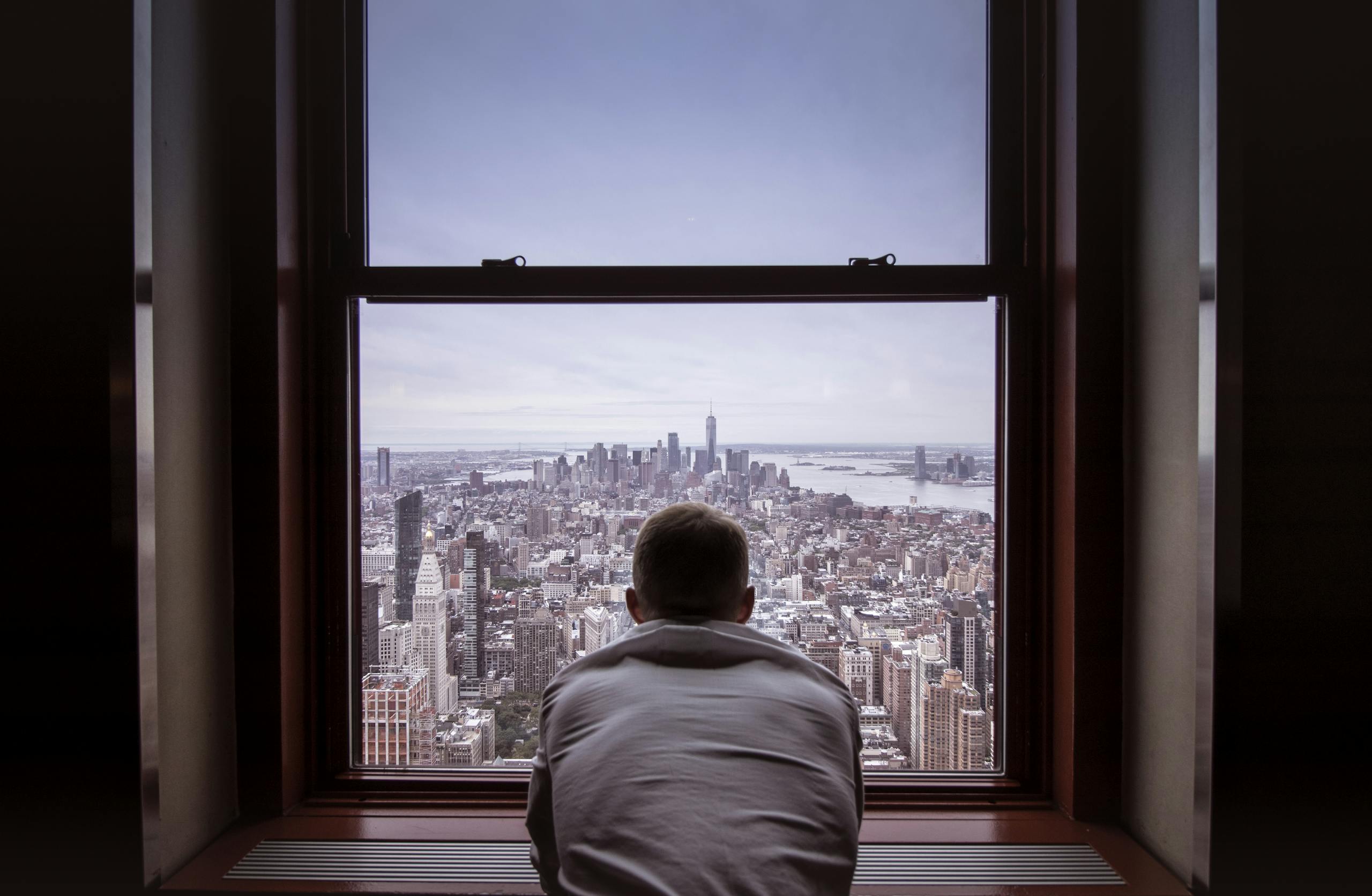 Man reflecting while overlooking New York City skyline through window
