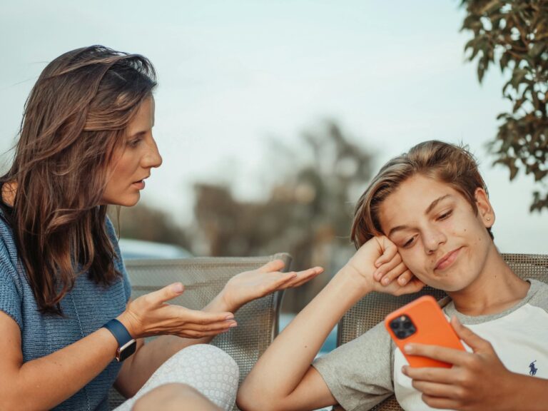 Mother engaging with teenage son holding smartphone outdoors