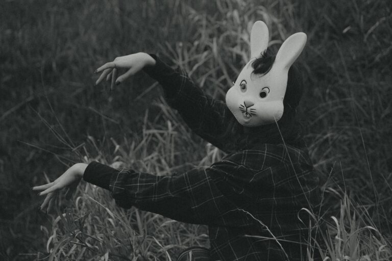 Mysterious figure in rabbit mask posing in tall grass creating eerie atmosphere.