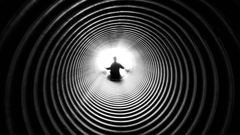 Person silhouetted against light at end of spiral tunnel