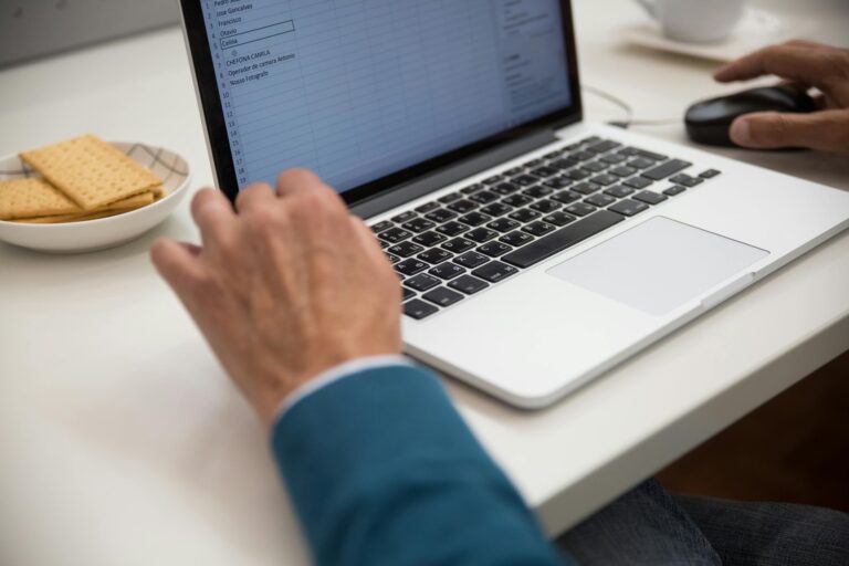 Person working focused on laptop at desk with snacks emphasizing productivity and technology.