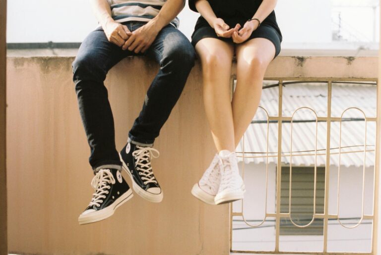 Relaxed couple sitting on ledge wearing stylish sneakers showcasing togetherness.