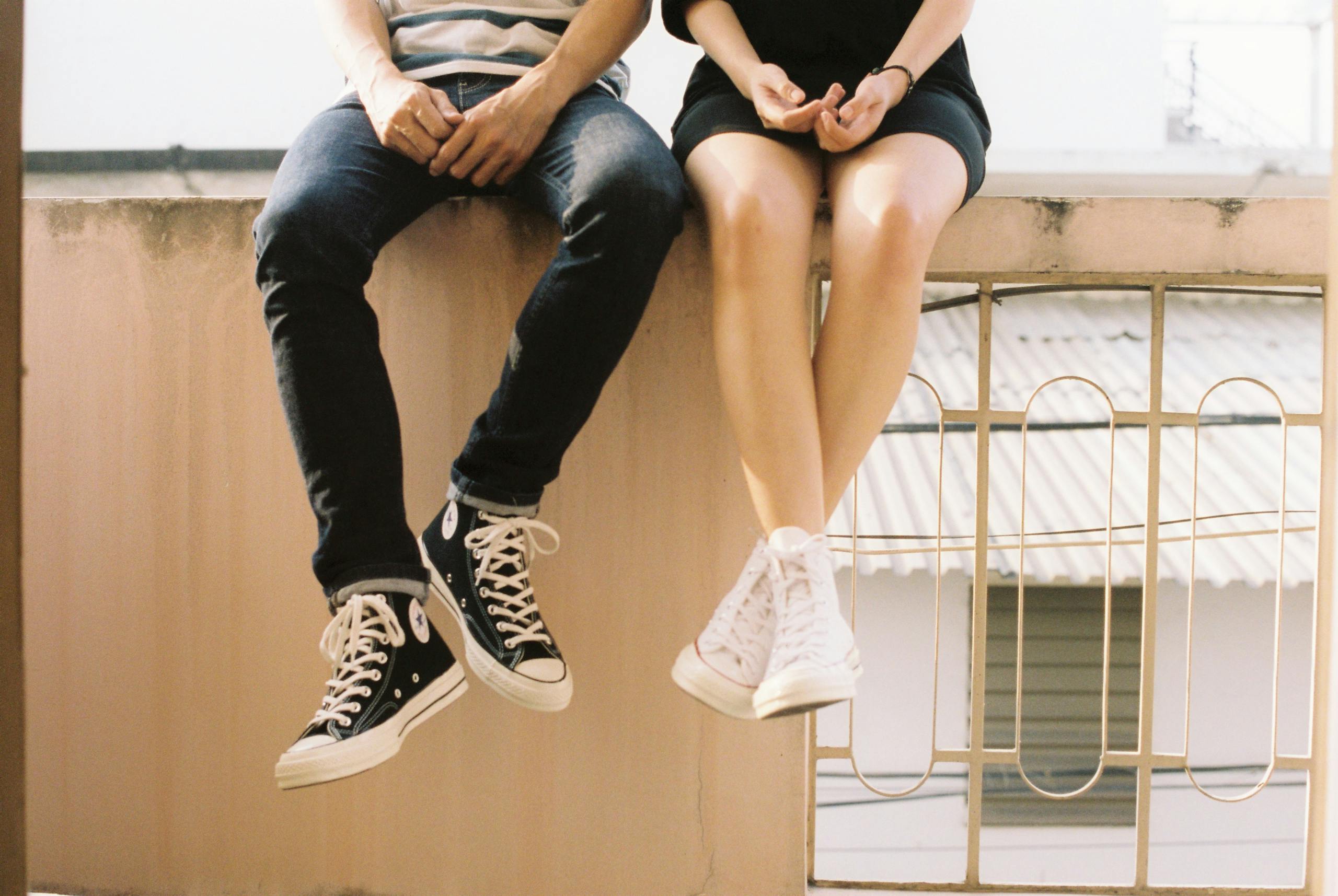 Relaxed couple sitting on ledge wearing stylish sneakers showcasing togetherness.
