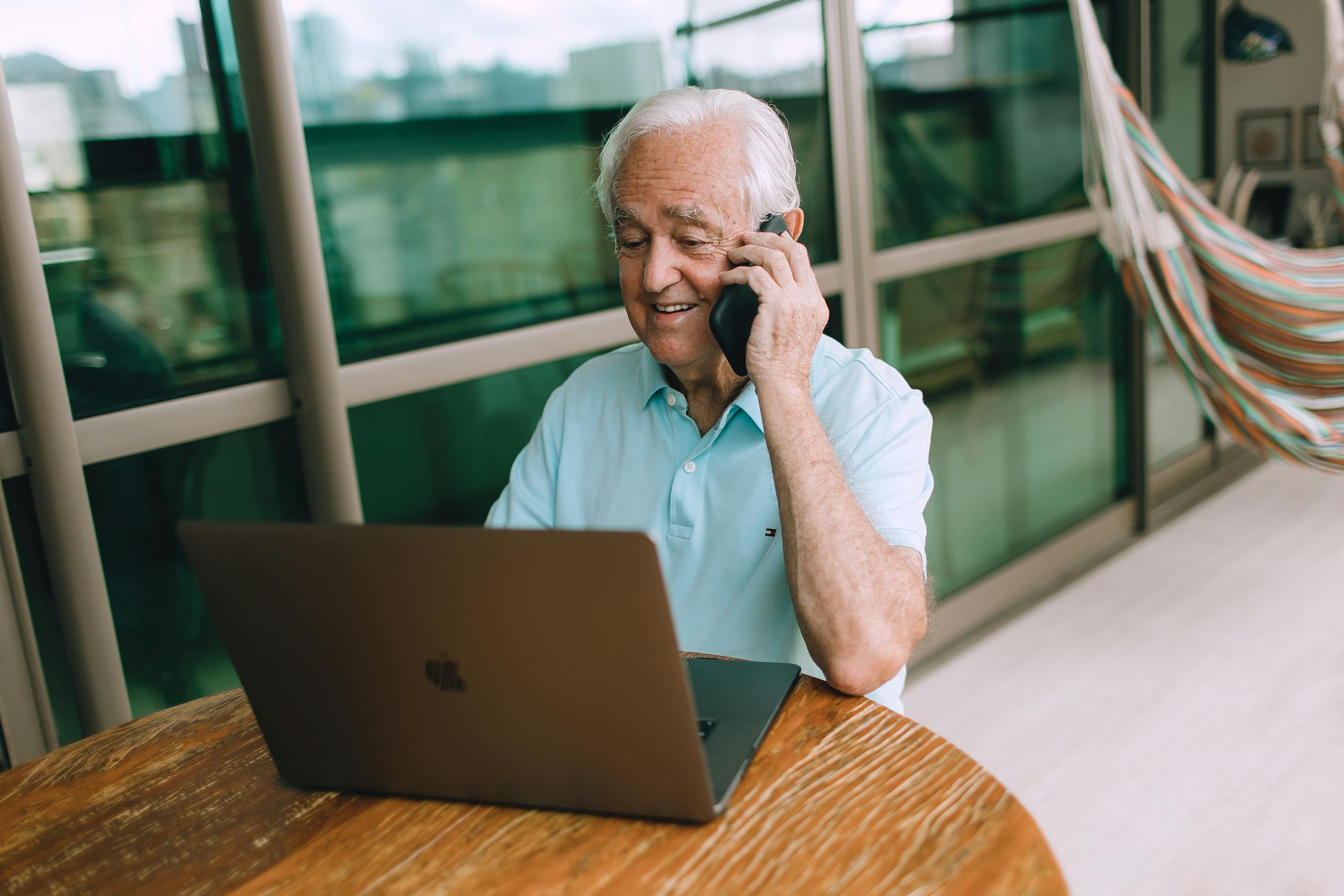 Senior man on phone call while working on laptop at home casually dressed