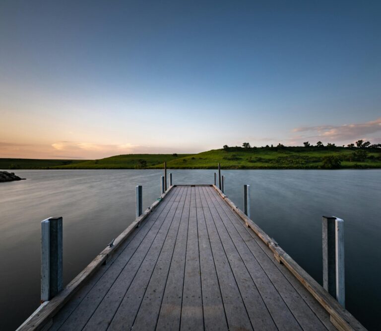 Serene wooden pier stretching into calm lake under picturesque sunset sky.