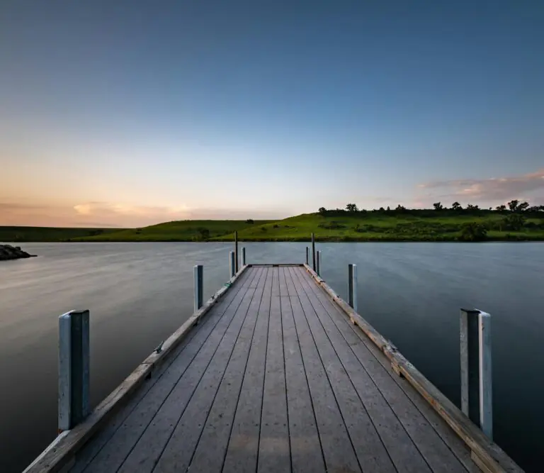 Serene wooden pier stretching into calm lake under picturesque sunset sky.