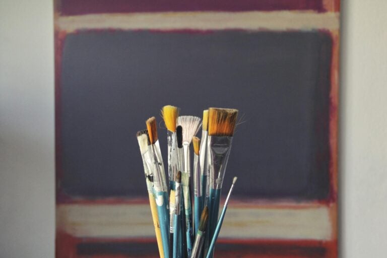 Paintbrushes displayed in front of abstract canvas showing creative inspiration