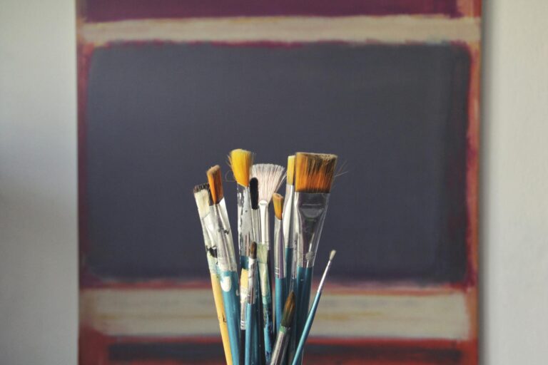 Paintbrushes displayed in front of abstract canvas showing creative inspiration