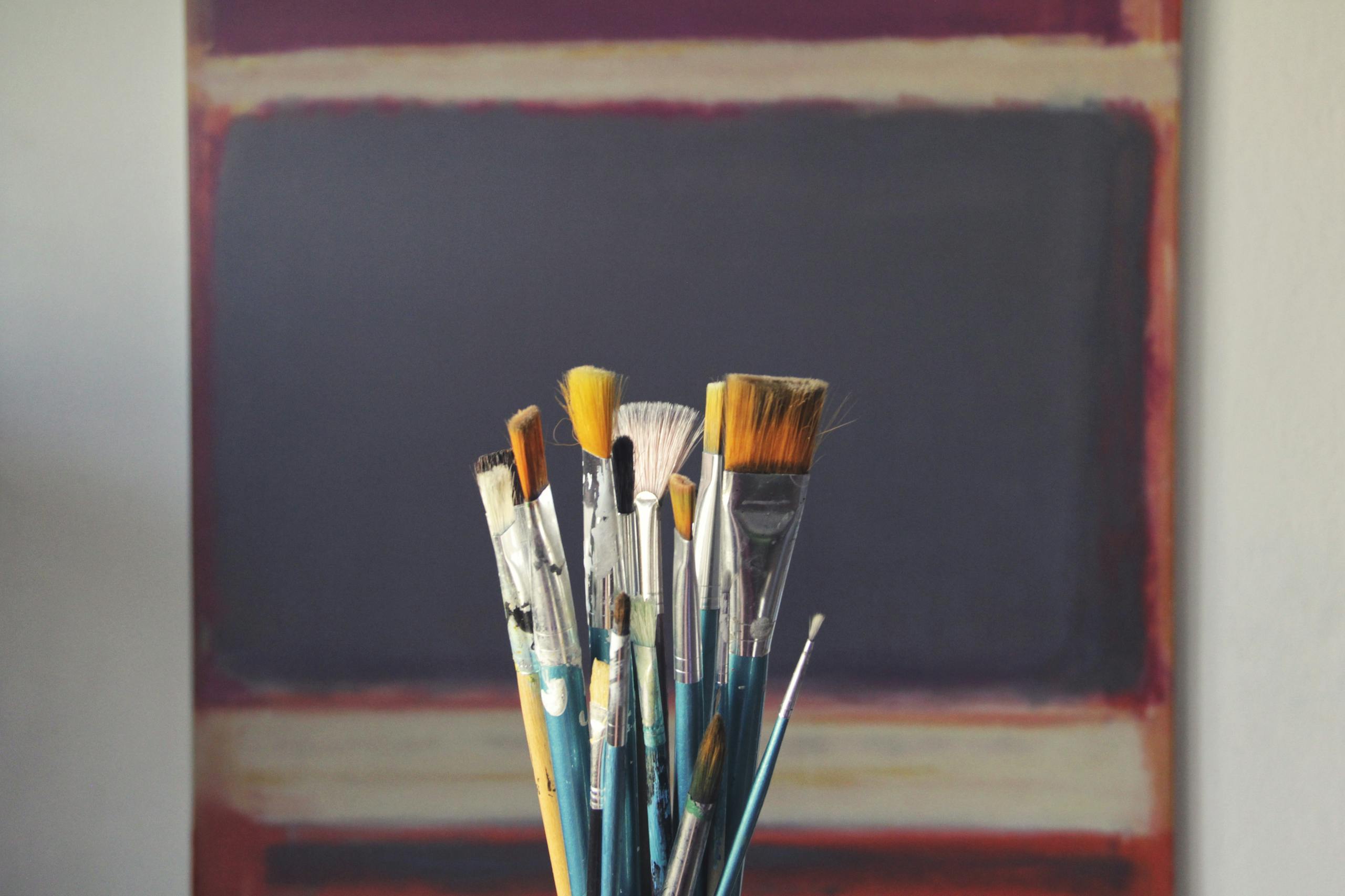 Paintbrushes displayed in front of abstract canvas showing creative inspiration