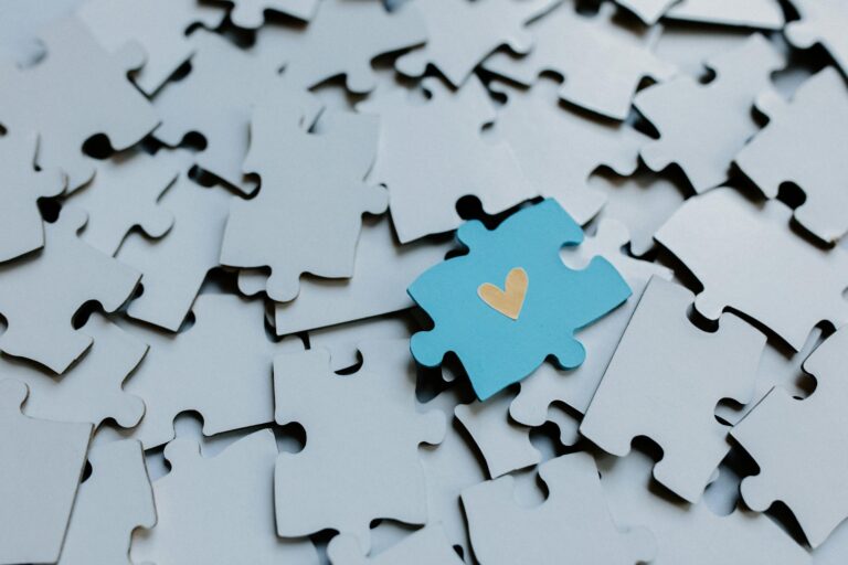 Single blue puzzle piece with heart amid scattered pieces symbolizing connection