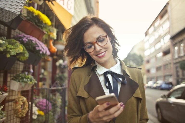 Smiling woman using phone outside colorful urban flower shop on sunny day