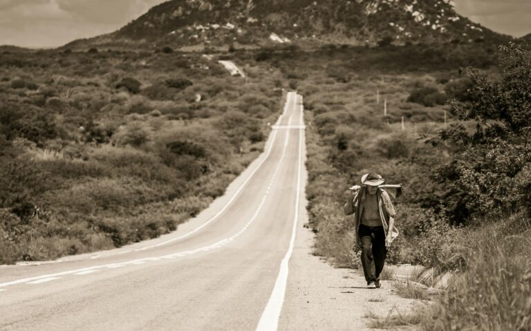 Solitary man walking along scenic rural road in Brazil beneath vast open sky.