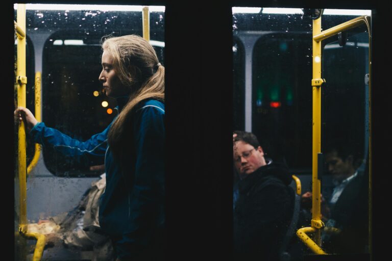 Solitary woman stands in dimly lit Dublin city bus during nightly commute.