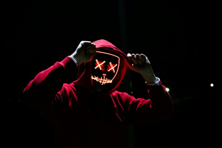 Spooky illuminated mask figure wearing red hoodie in darkness