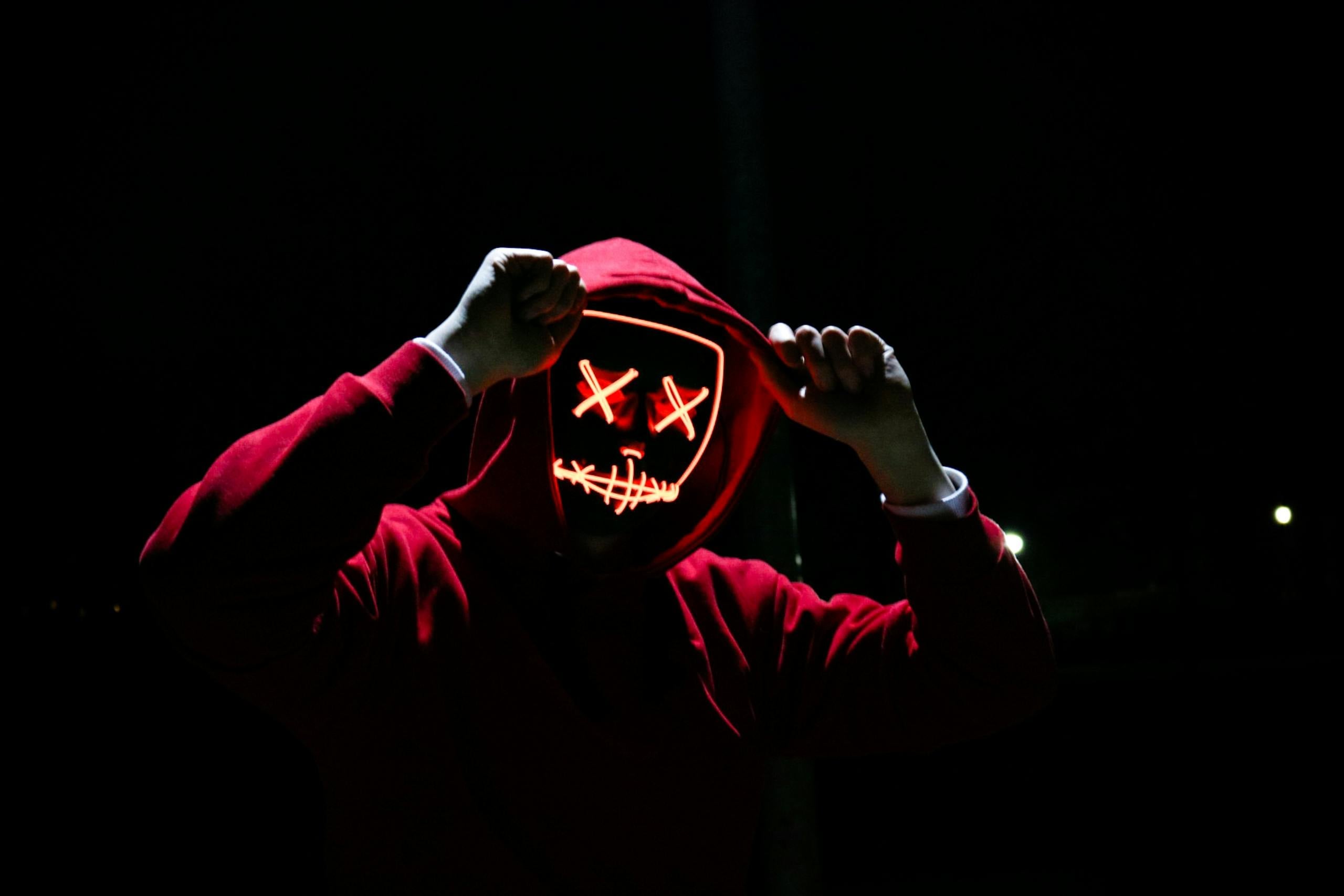 Spooky illuminated mask figure wearing red hoodie in darkness