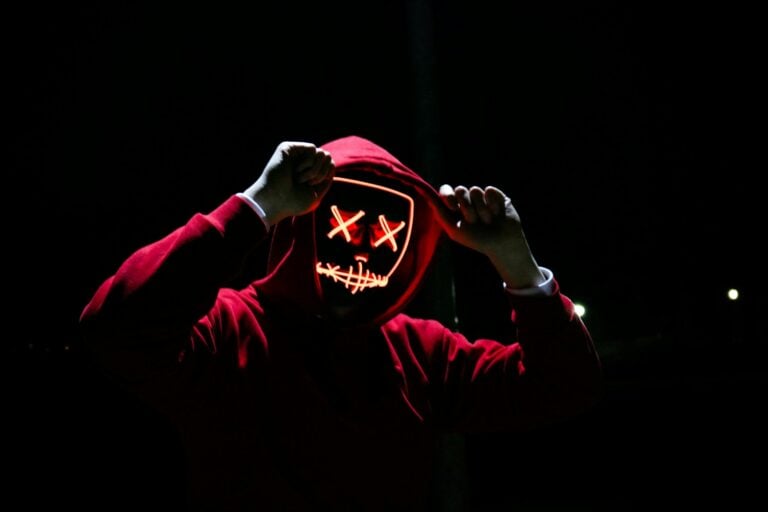Spooky illuminated mask figure wearing red hoodie in darkness