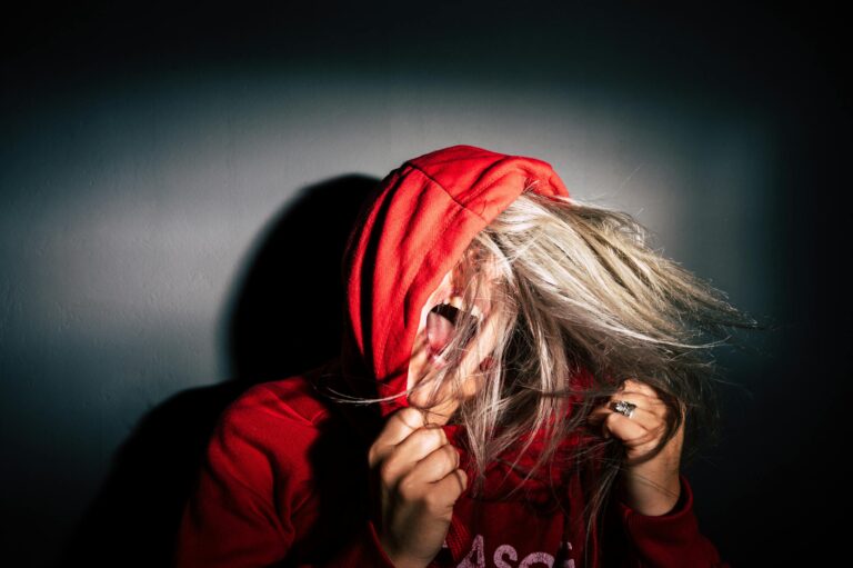 Teenager in red hoodie screams with hair flying conveying intense emotion.