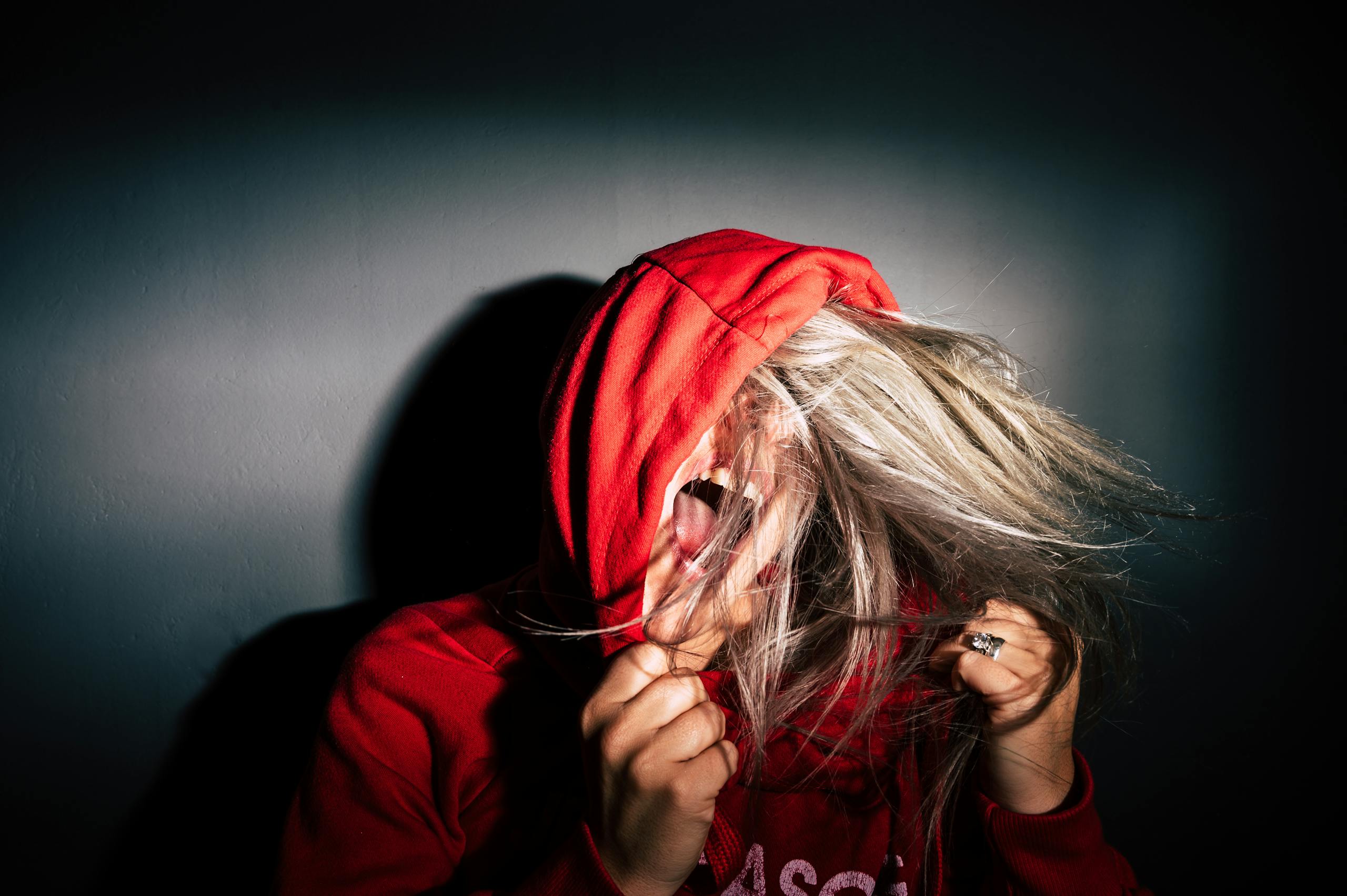 Teenager in red hoodie screams with hair flying conveying intense emotion.