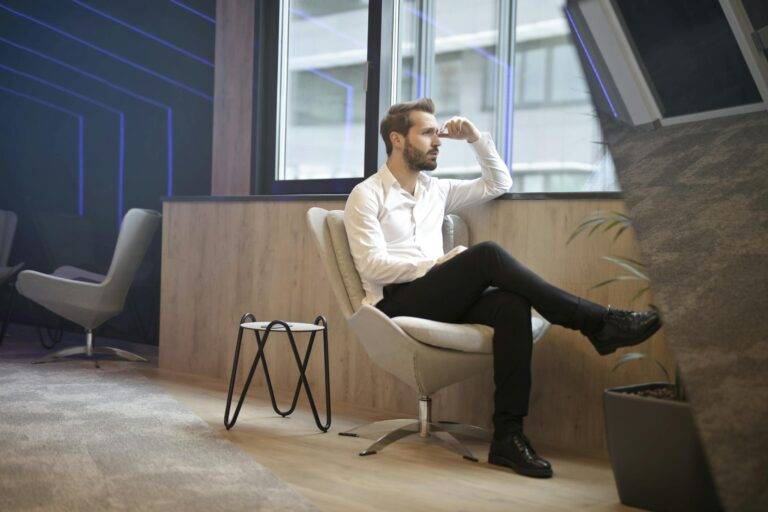 Thoughtful man in modern office interior sitting and looking outside window.