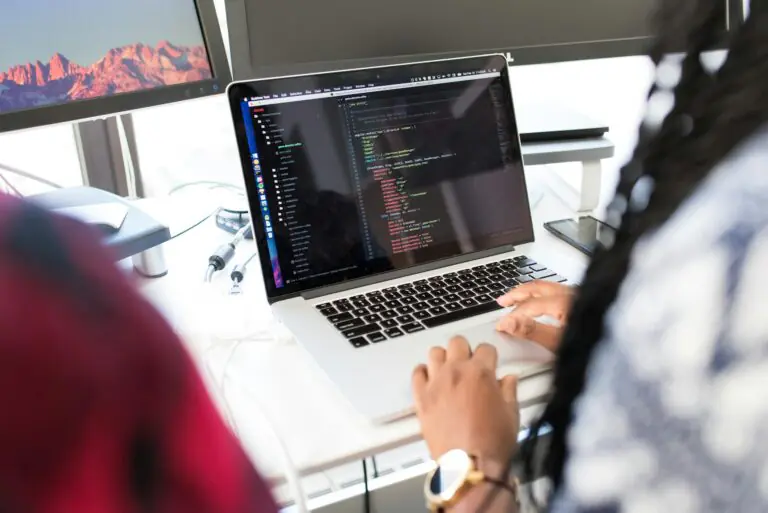 Woman coding on laptop in modern office environment with multiple monitors displayed