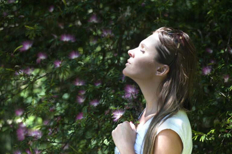 Woman enjoying serene moment in sunlit garden surrounded by vibrant flowers.