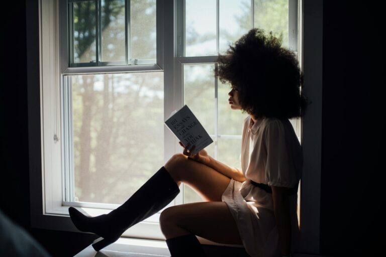 Woman reading peacefully by window with natural light streaming in.