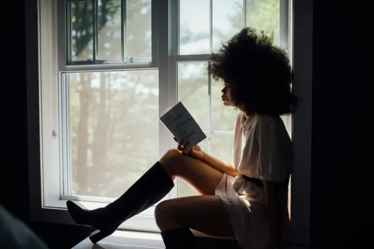 Woman reading peacefully by window with natural light streaming in.
