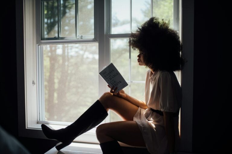 Woman reading peacefully by window with natural light streaming in.