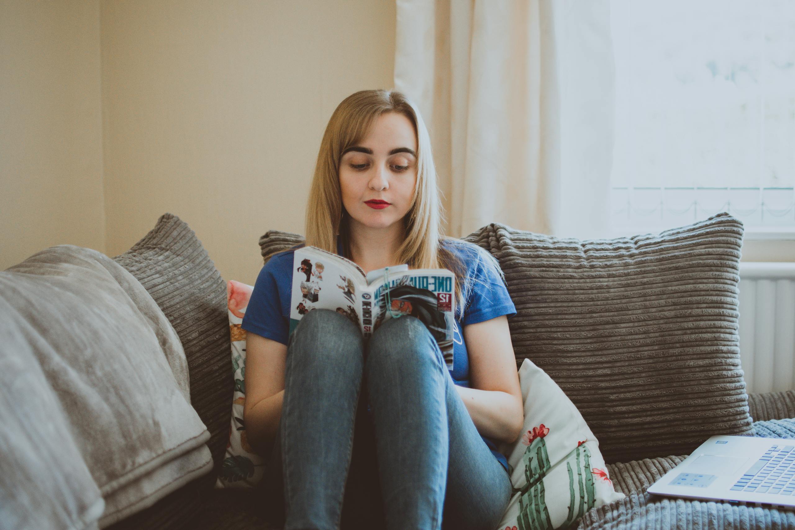 Woman relaxing on sofa reading manga in peaceful, comfortable setting