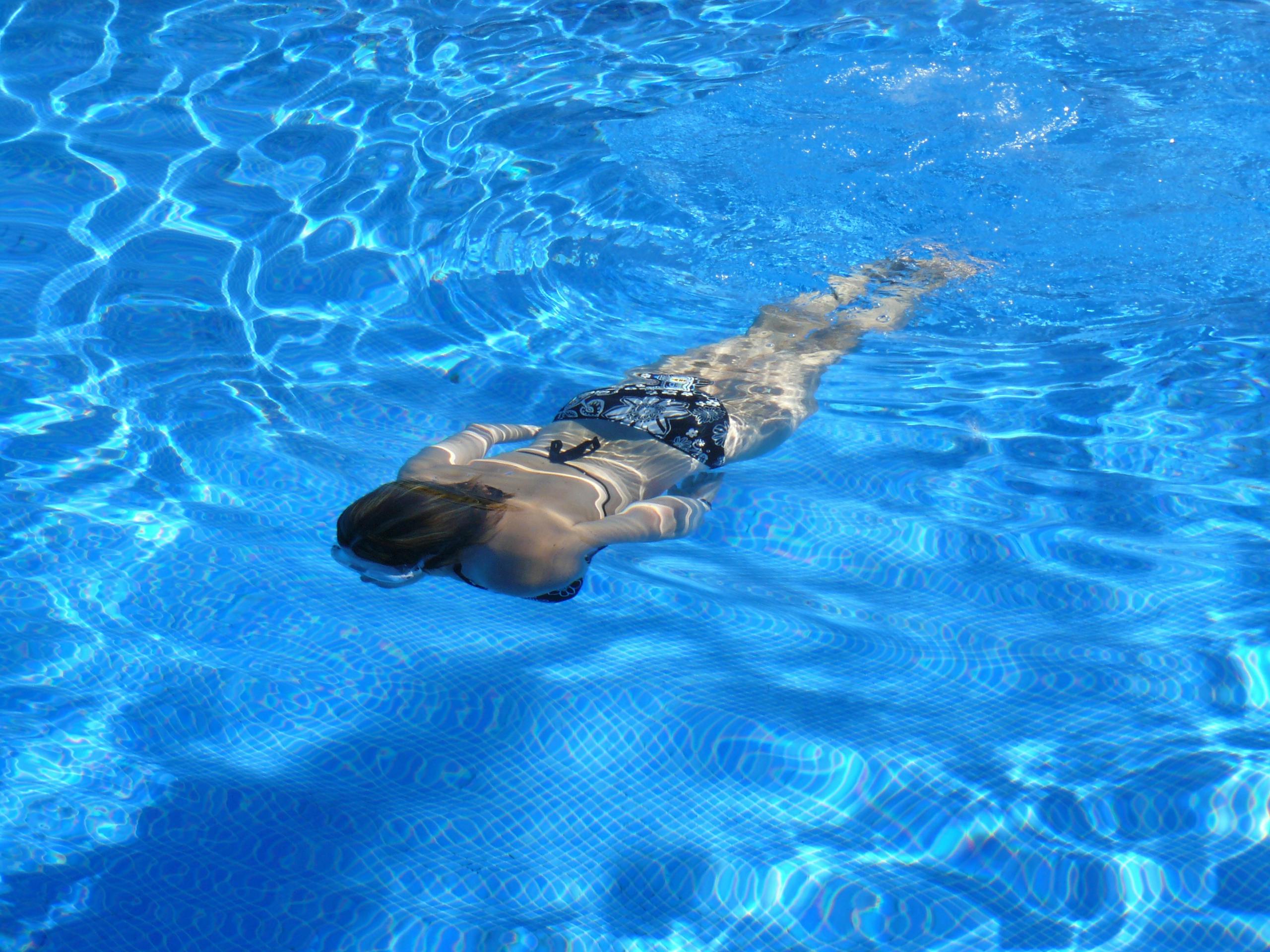 Woman swimming freestyle underwater in sunlit pool with graceful form.