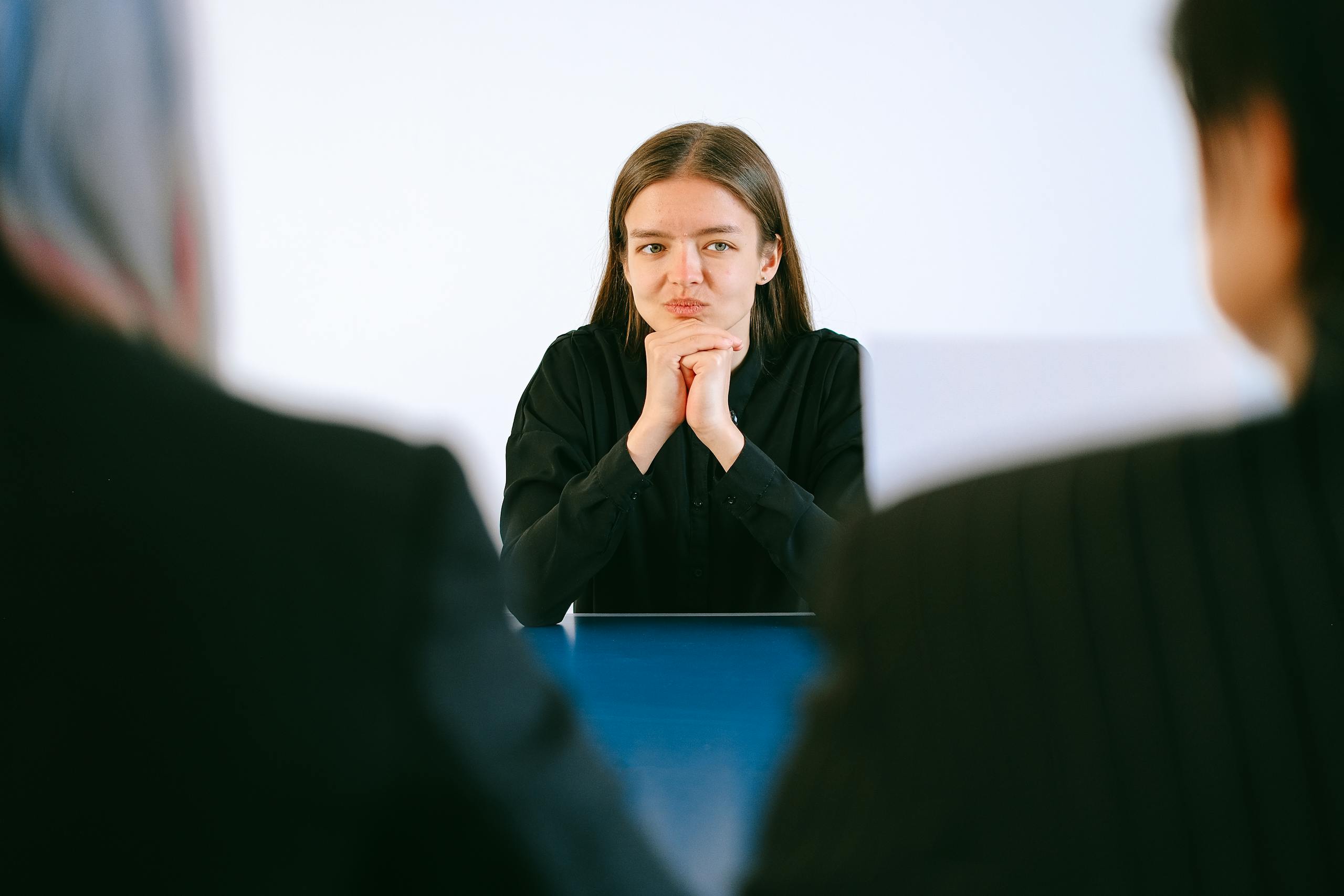 Woman in job interview maintaining focused intensity across table from two interviewers.