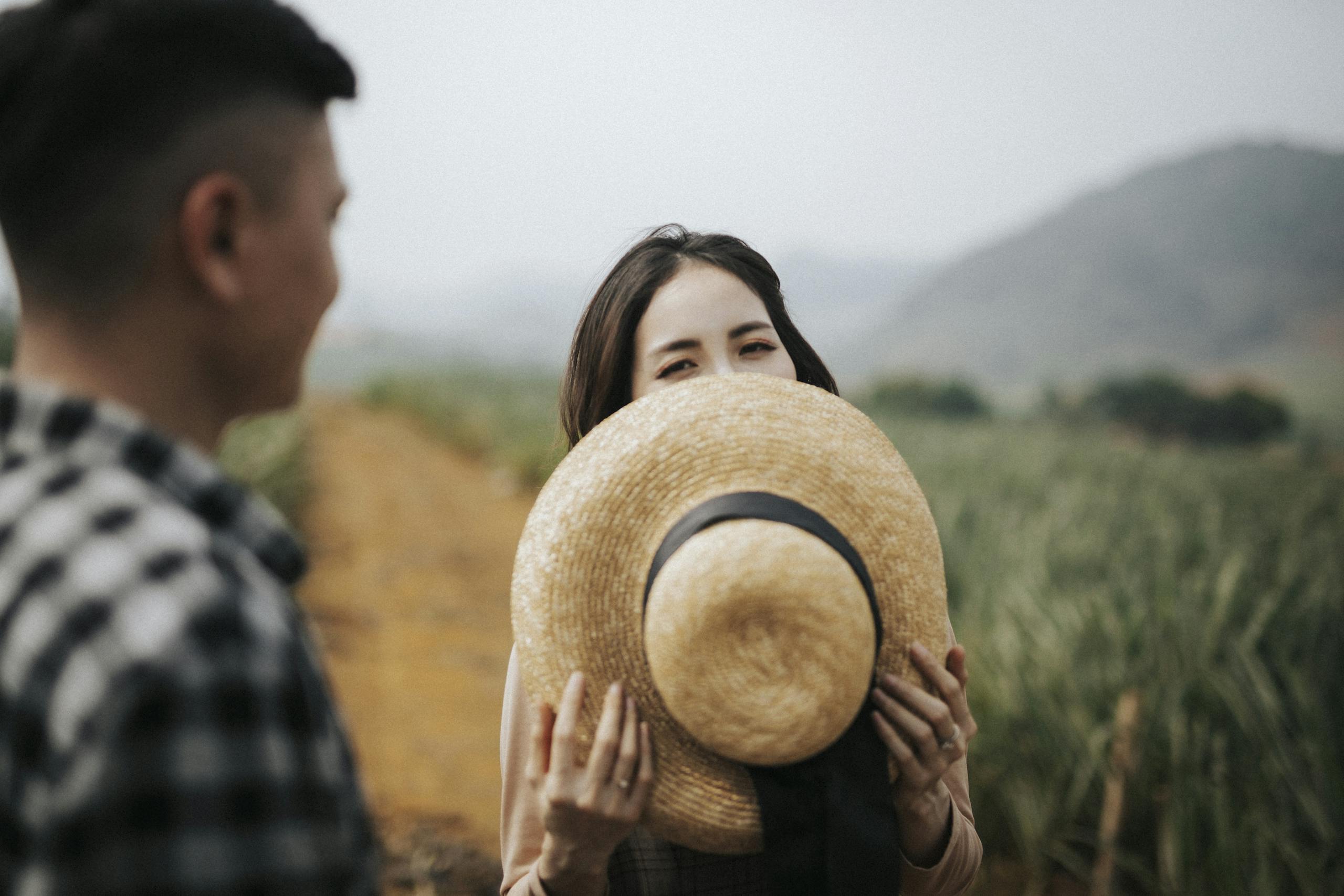 Young woman playfully hides behind straw hat in vietnamese field candid moment