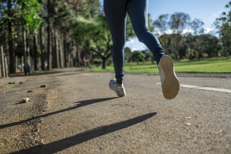 Woman running outdoors on sunny day along scenic park trail focusing on fitness