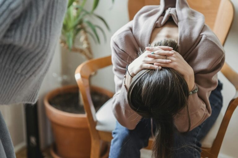 Woman sitting with head in hands indoors expressing distress and emotional turmoil.
