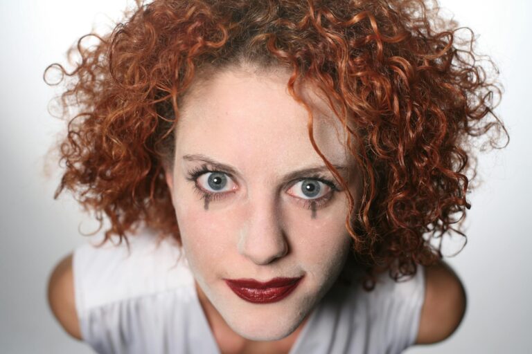 Woman with curly red hair and dramatic clown makeup posing boldly upwards