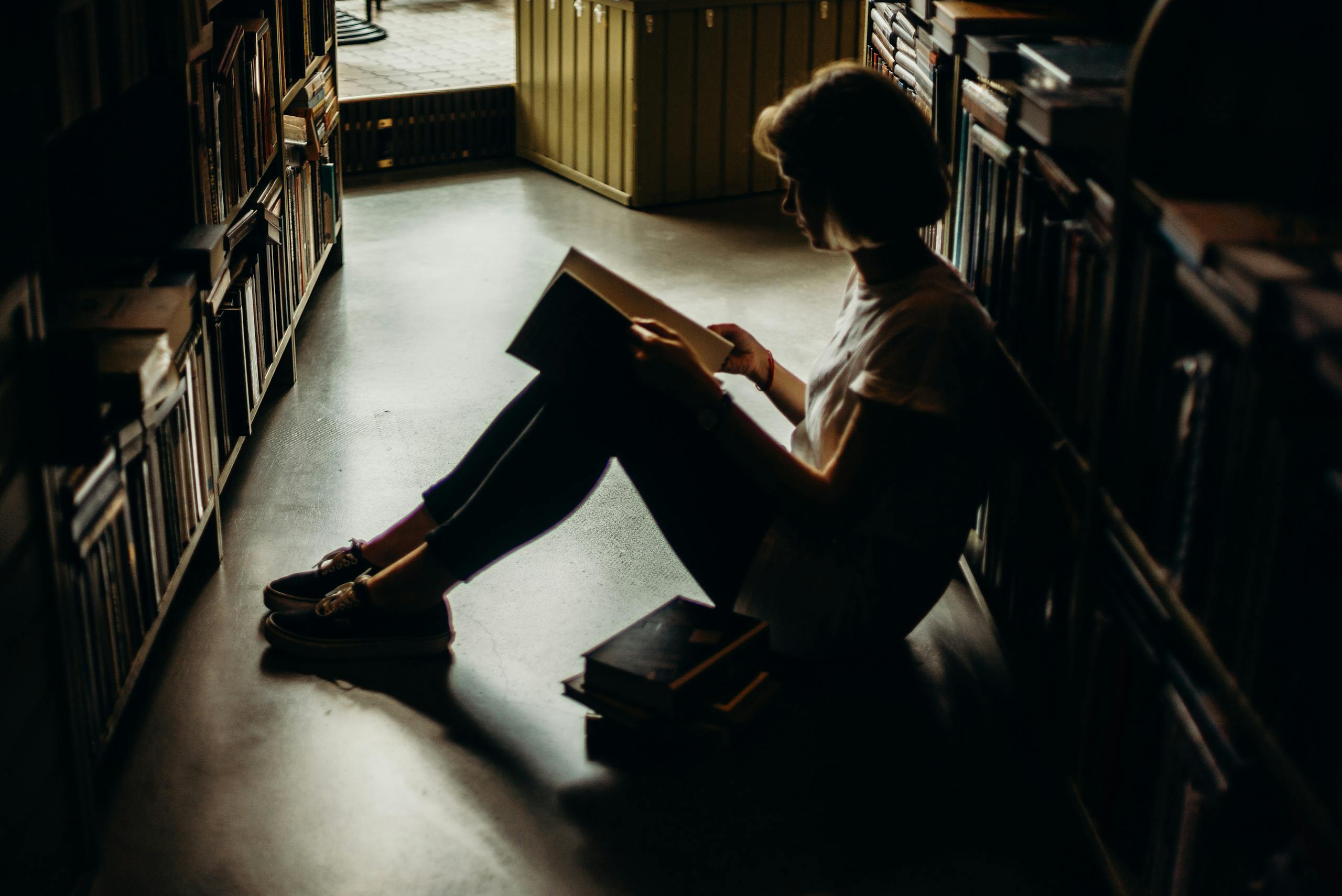 Young woman engrossed in book sitting on floor of quiet library creating cozy reading atmosphere