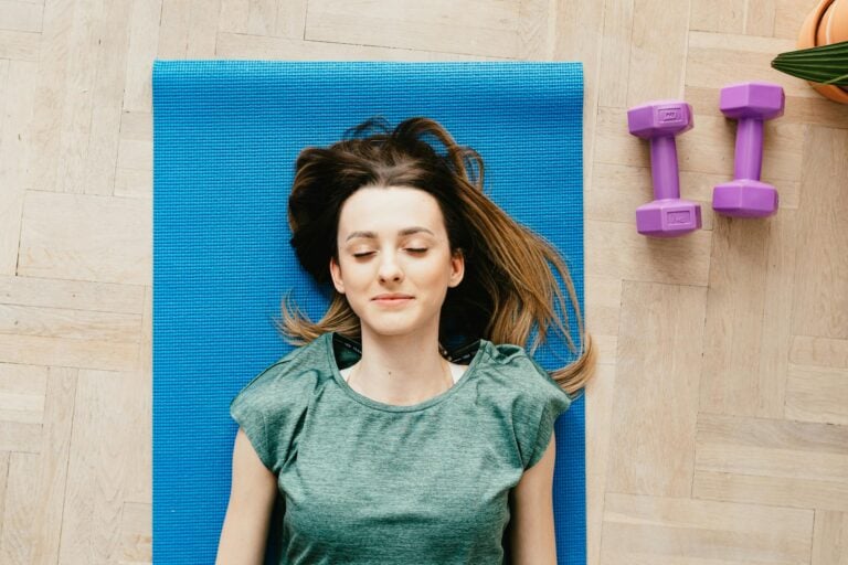 Young woman peacefully resting on a yoga mat with dumbbells beside her indoors