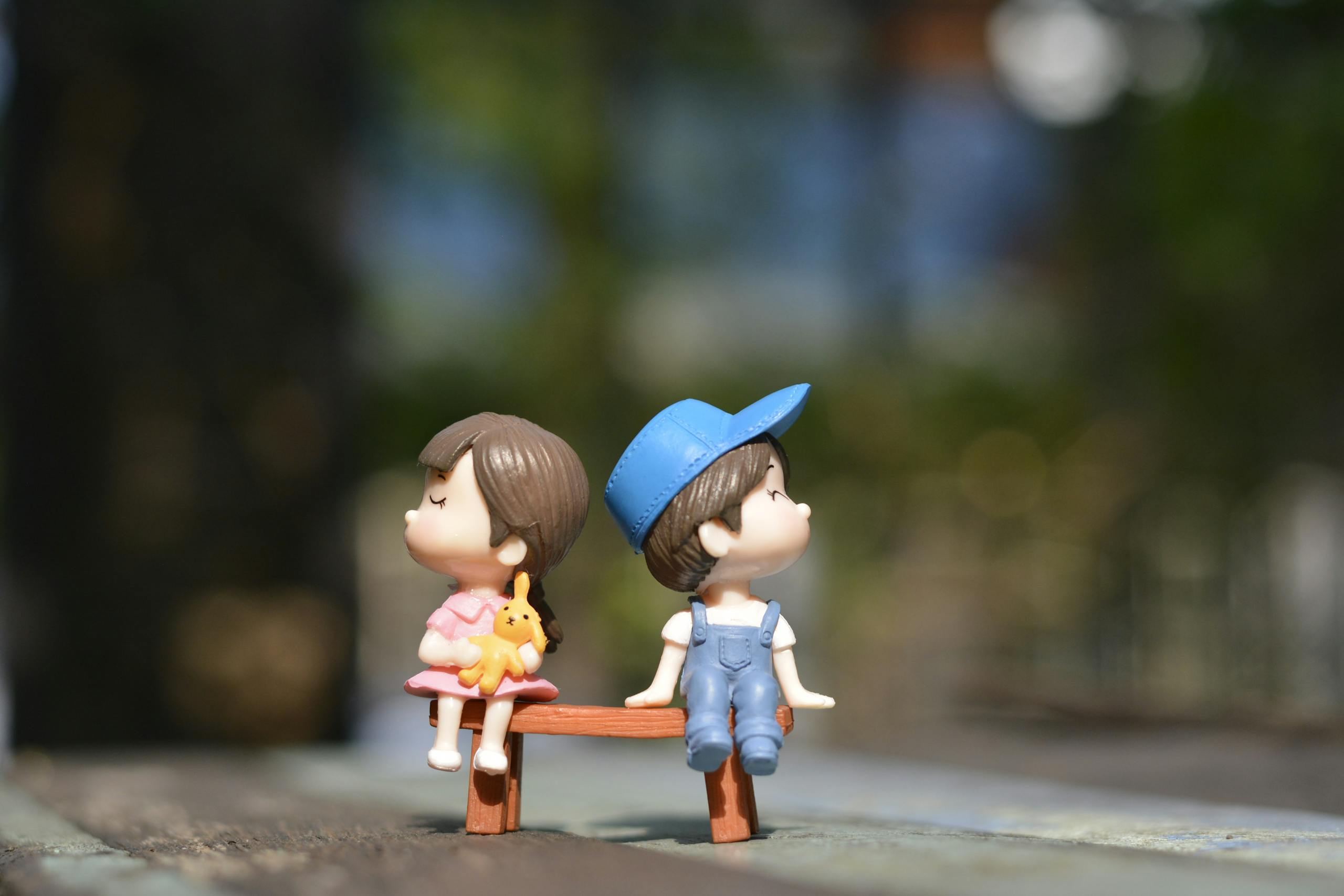 Decorative figurines of boy and girl sitting together on sunny bench.