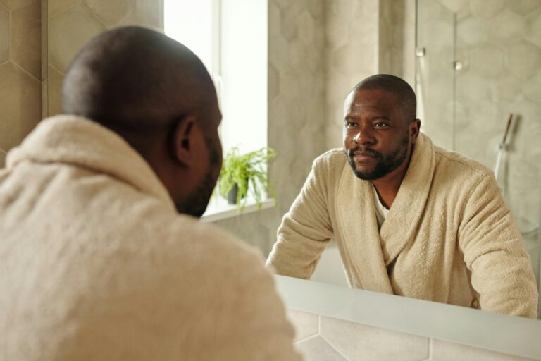 Adult man in bathrobe reflecting in bathroom mirror during morning routine