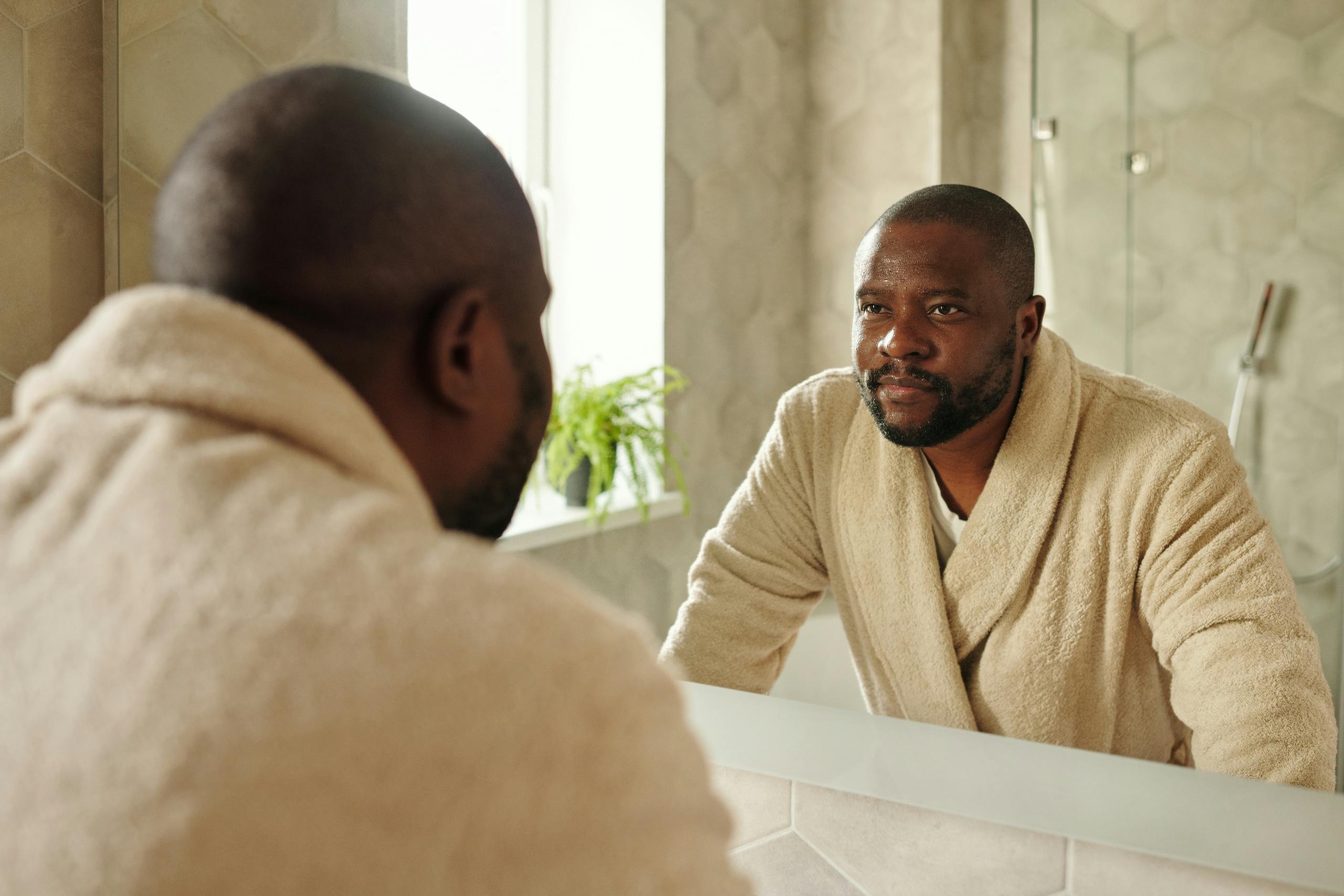 Adult man in bathrobe reflecting in bathroom mirror during morning routine